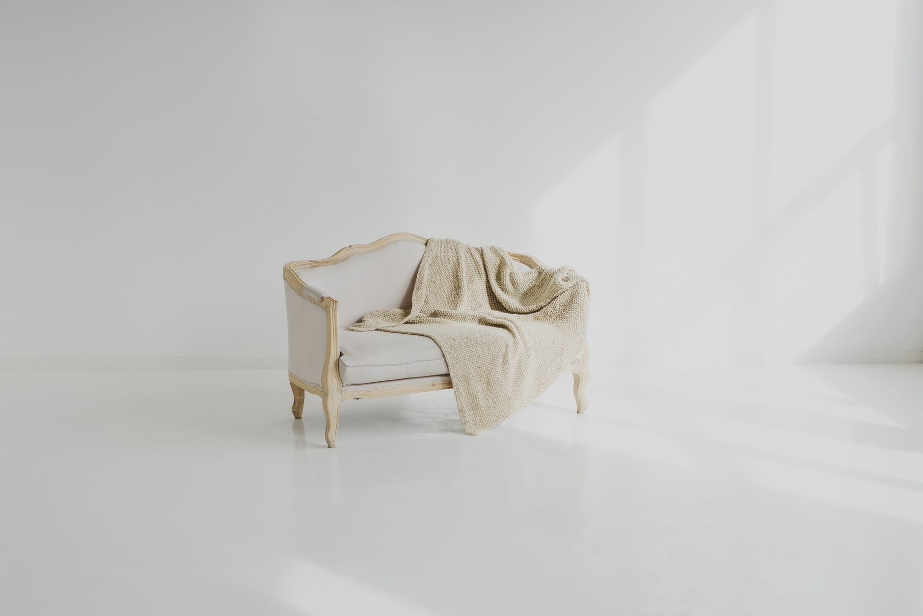 A softly styled, light-filled living room by Studio Nook — a cream settee with a warm knit throw.