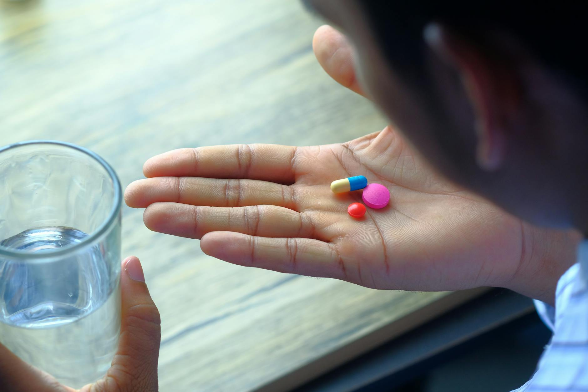 Person taking a daily supplement with a glass of water